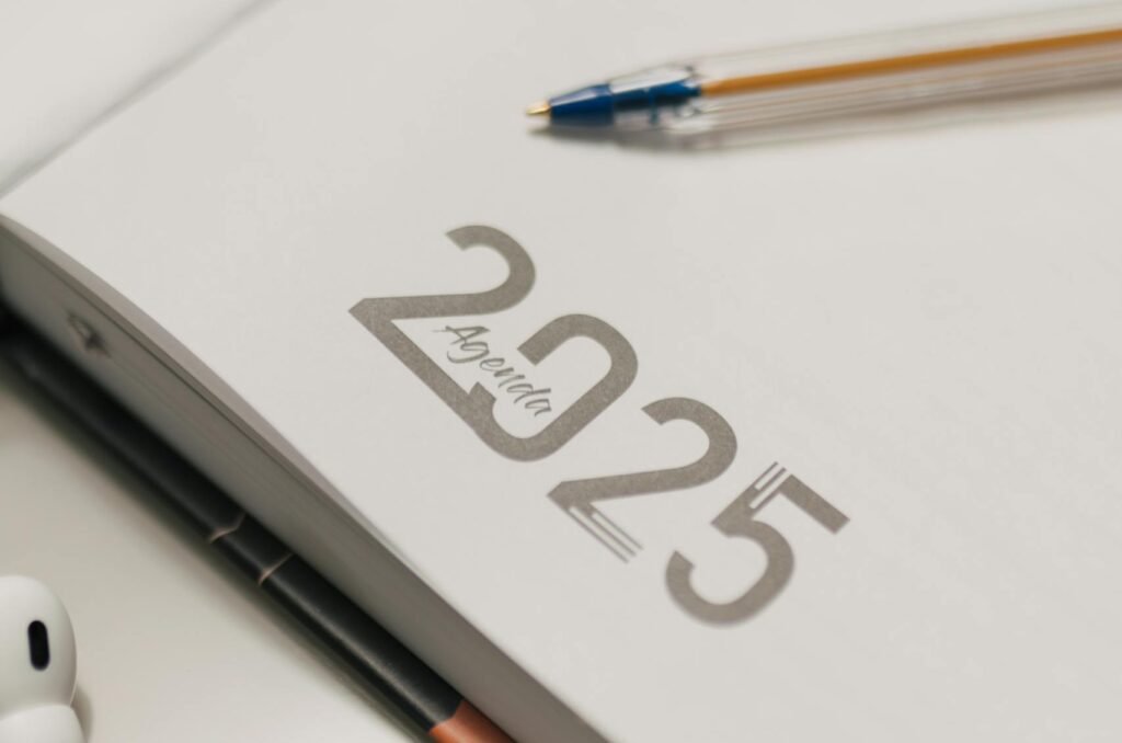 Close-up of 2025 planner with AirPods and pen on desk.